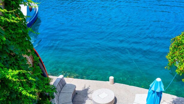 Una terraza de piedra con un área de estar circular, una sombrilla azul y vista al agua.