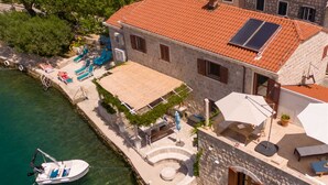 Una propiedad costera con un barco amarrado, un edificio de piedra con techo de tejas y una pequeña zona de piscina.
