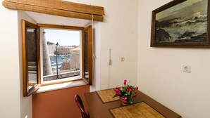 A room with a view of a harbor, a wooden table with a vase of flowers, and a framed painting on the wall. - Studio Lončarica next to Revelin (Dubrovnik)