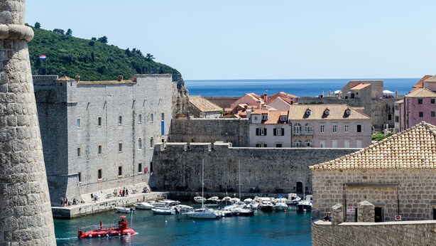 A historic waterfront area with stone buildings, a harbor with boats, and a clear view of the sea. - Studio Lončarica next to Revelin (Dubrovnik)
