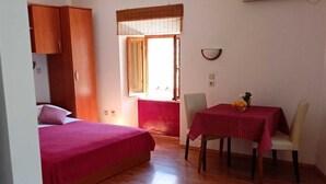 A room with a bed, a table with a red tablecloth, a window with a view, and a ceiling fan. - Studio Lončarica next to Revelin (Dubrovnik)