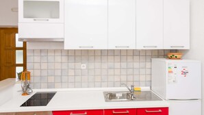 Eine Küche mit weißen Schränken, einer Edelstahl-Spüle, einem eingebauten Ofen und einem kleinen Kühlschrank.