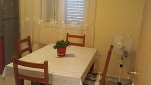 Un comedor con mesa, sillas, una planta en maceta, un ventilador y una ventana con persianas.