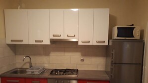 Una cocina con armarios superiores blancos, un refrigerador de acero inoxidable, un microondas, una estufa a gas y un lavamanos.