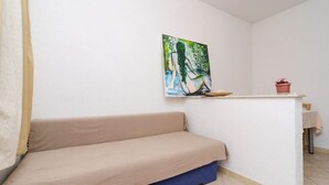 Een kamer met een beige bank, een kleine tafel met een plant in pot, en een schilderij aan de muur.