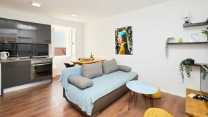 Eine moderne Wohnung mit Küchenzeile, einem Sofa, einem kleinen Esstisch und einem einzelnen Sessel.
