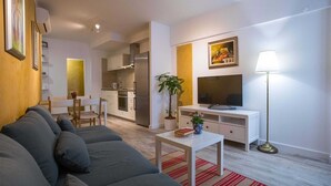 Una sala de estar moderna con un sofá gris, una zona de comedor con una mesa blanca y una cocina con armarios blancos.