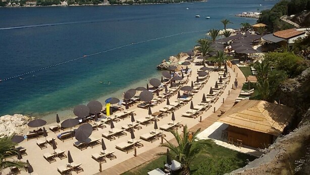 Un complejo turístico en la playa con tumbonas y sombrillas, piscina y vistas al mar.