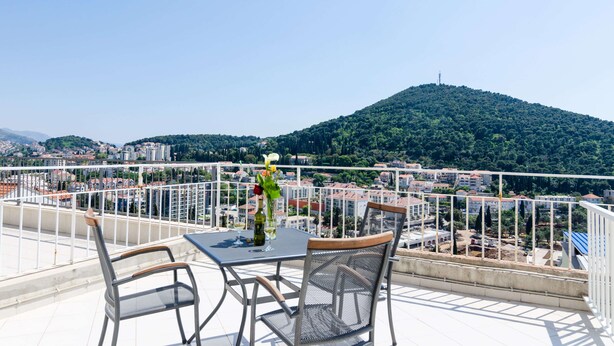 Un balcon avec une table et des chaises, offrant une vue sur le paysage urbain et une colline.
