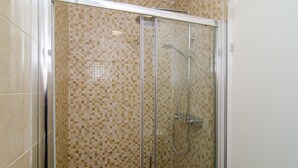 Ducha con cerramiento de vidrio y pared con mosaico de azulejos.