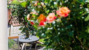 Una mesa metálica redonda con una botella y un vaso, rodeada de follaje y rosas.