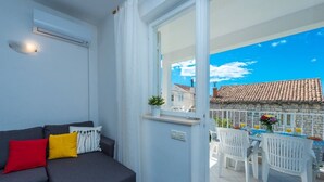 Ein modernes Wohnzimmer mit einem grauen Sofa, einem kleinen Tisch mit einer Vase und Blumen sowie einem Balkon mit weißen Stühlen und einem Esstisch.