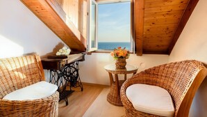 A cozy room with a sloped ceiling, wooden beams, a view of the sea, wicker furniture, and a sewing machine. - Daniela Old Town three bedroom apartment (Dubrovnik)