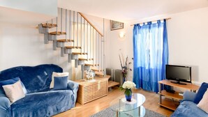 A modern living room with a blue sofa, a glass coffee table, a TV on a wooden stand, and a staircase with wooden steps. - Daniela Old Town three bedroom apartment (Dubrovnik)