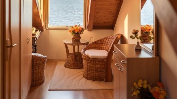 A cozy cabin interior with a wooden ceiling, a small dining area with wicker furniture, and a view of the ocean through a window. - Daniela Old Town three bedroom apartment (Dubrovnik)