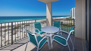 A balcony with a round table and four chairs, overlooking a beach and ocean.