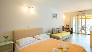 Ein Hotelzimmer mit Bett, Sofa, Schreibtisch und Stuhl. Ein Fenster mit Vorhängen bietet einen Blick ins Freie.