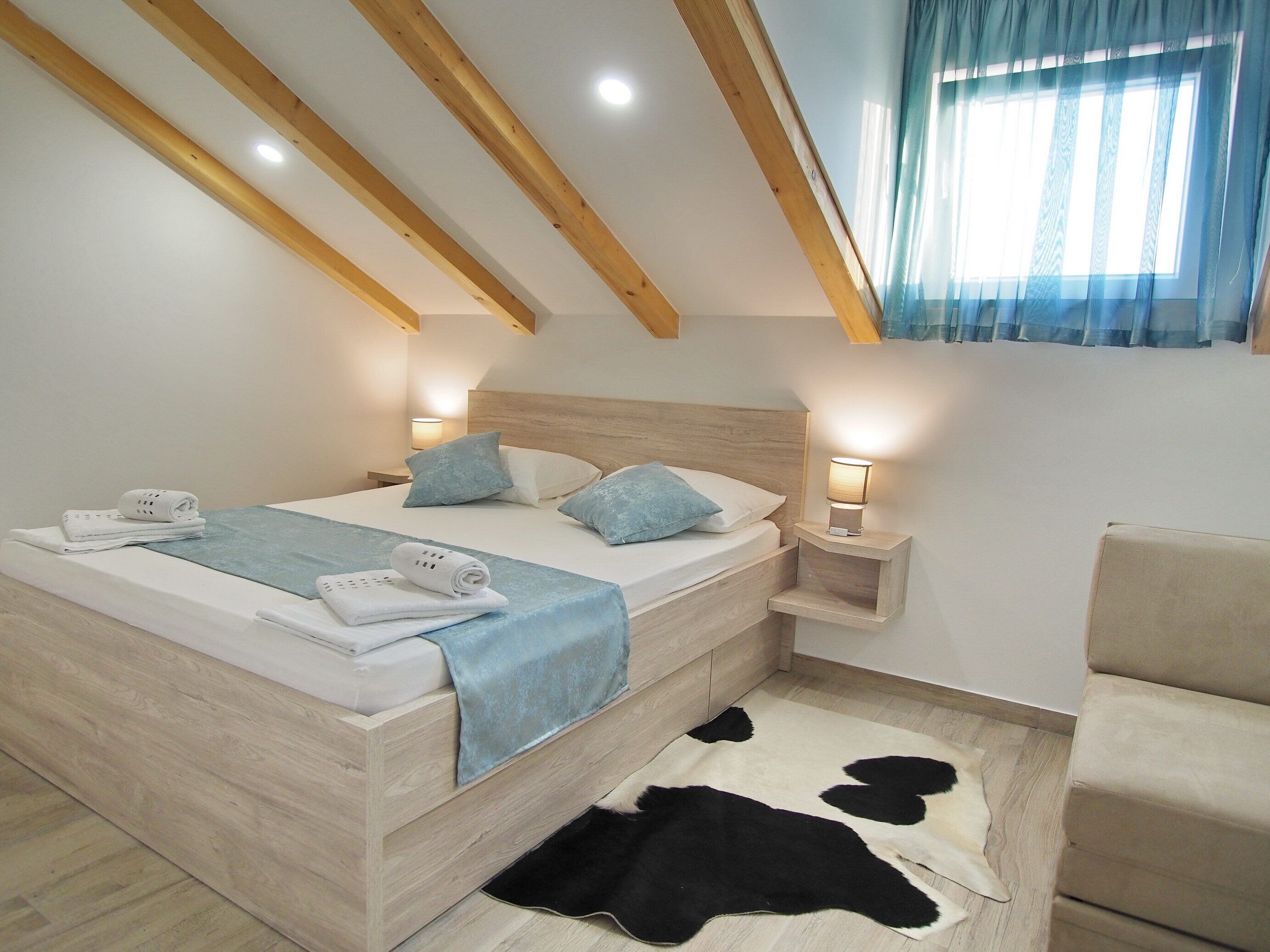 A bedroom with a wooden ceiling, a bed with a blue blanket, two bedside lamps, and a cowhide rug.