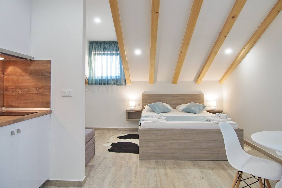 Une chambre avec un plafond en bois, un lit avec des oreillers, une table de chevet avec une lampe, une chaise blanche et un banc en bois.