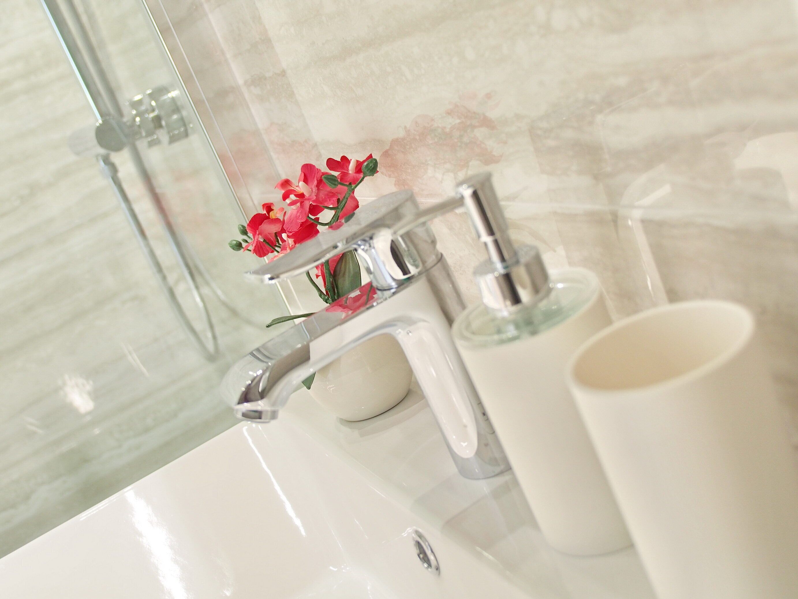 A bathroom with a white sink, a mirror, a faucet, and a soap dispenser.