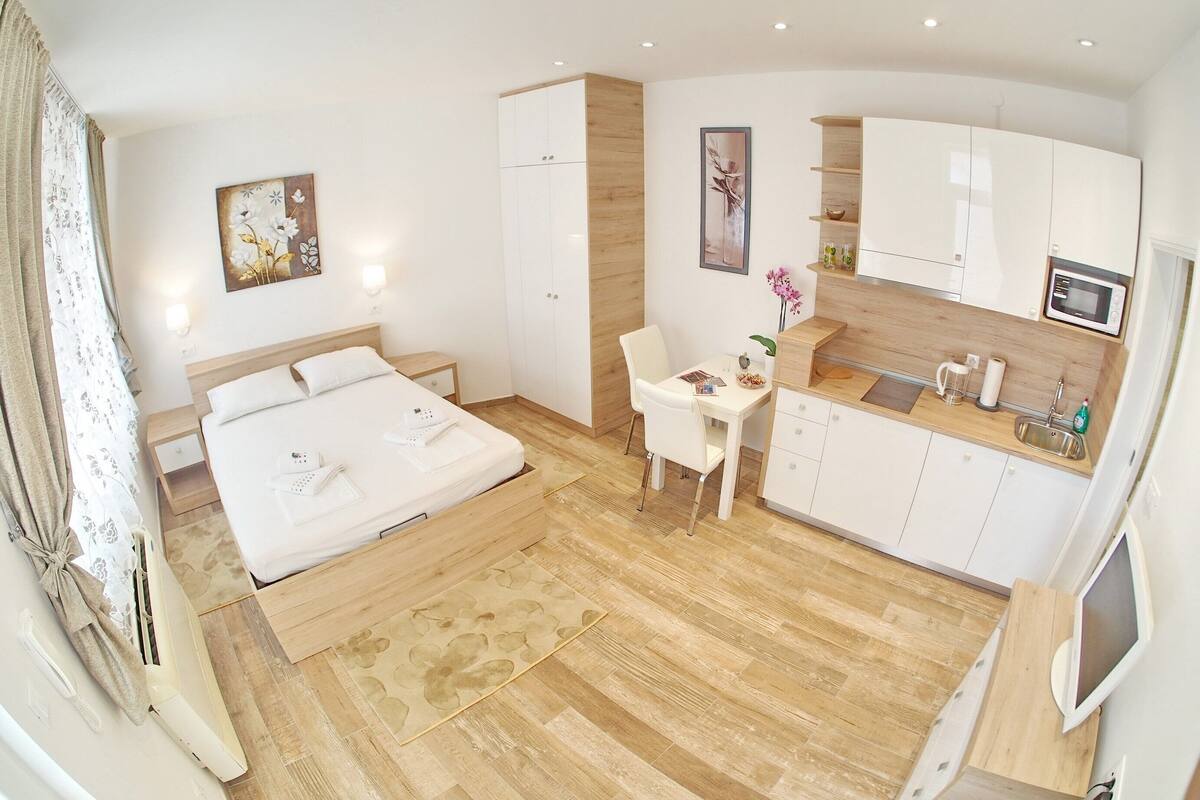 Une chambre d’hôtel moderne équipée d’un lit, d’une petite table à manger, d’un coin cuisine et d’un téléviseur.