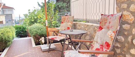 Une terrasse extérieure avec une table ronde et deux chaises, un parasol blanc et un mur en pierre.