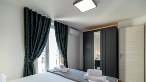 Habitación de hotel con cama, cortinas oscuras, un armario y vistas por la ventana.
