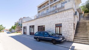 Un edificio de dos pisos con fachada de piedra, un coche azul estacionado al frente y una escalera que conduce al piso superior.