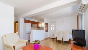 Ein modernes Wohnzimmer mit Sofa, Couchtisch, Fernseher und Essbereich mit Stühlen und Tisch.
