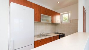 Eine moderne Küche mit Holzschränken, einem weißen Kühlschrank, einer Mikrowelle, einem Spülbecken und einem Fenster.