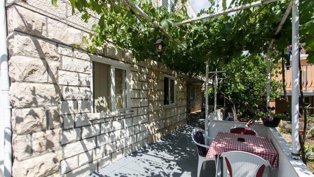 Un edificio de piedra con un pequeño patio al aire libre, una mesa cubierta con un mantel a cuadros y una silla.