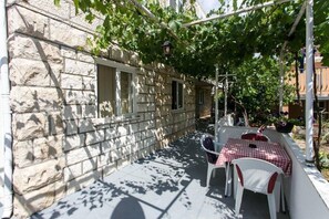 A stone building with a narrow outdoor patio, a table with a checkered tablecloth, and a chair. - Lovely 2bedroom apt on Batala,Lapad (Dubrovnik)