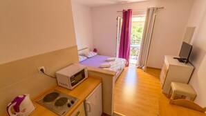 Una habitación de hotel compacta con kitchenette, una cama, un escritorio pequeño y un televisor.