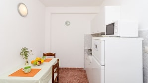 Une petite cuisine avec un réfrigérateur blanc, un four à micro-ondes et une table à manger agrémentée d’un vase et de fruits.