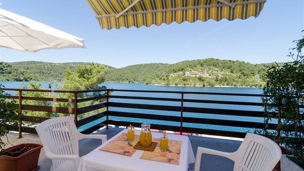 Une terrasse avec une table dressée pour deux personnes, donnant sur un lac et bordée d’une colline boisée en arrière-plan.