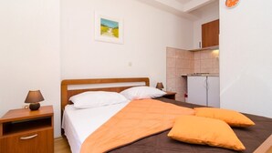 Une chambre à coucher avec un lit en bois, des oreillers blancs, une couverture orange, une table de chevet avec une lampe et une petite armoire.