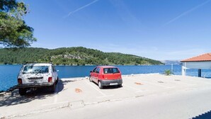 Un aparcamiento con dos coches, una masa de agua y una colina al fondo.