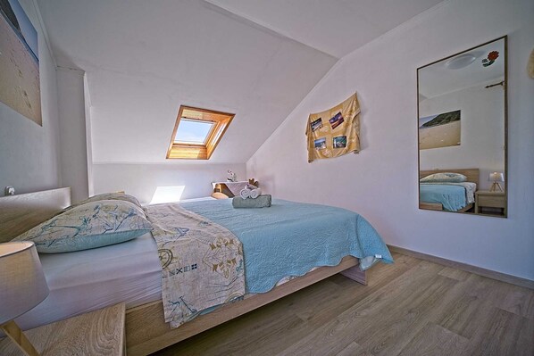 Une chambre à coucher comprenant un lit, une table de chevet, un miroir, une fenêtre et un mur orné d’un collage encadré.