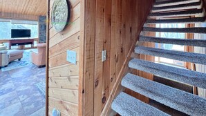 A wooden interior with a stone staircase, a television in the living area, and a decorative wall piece.
