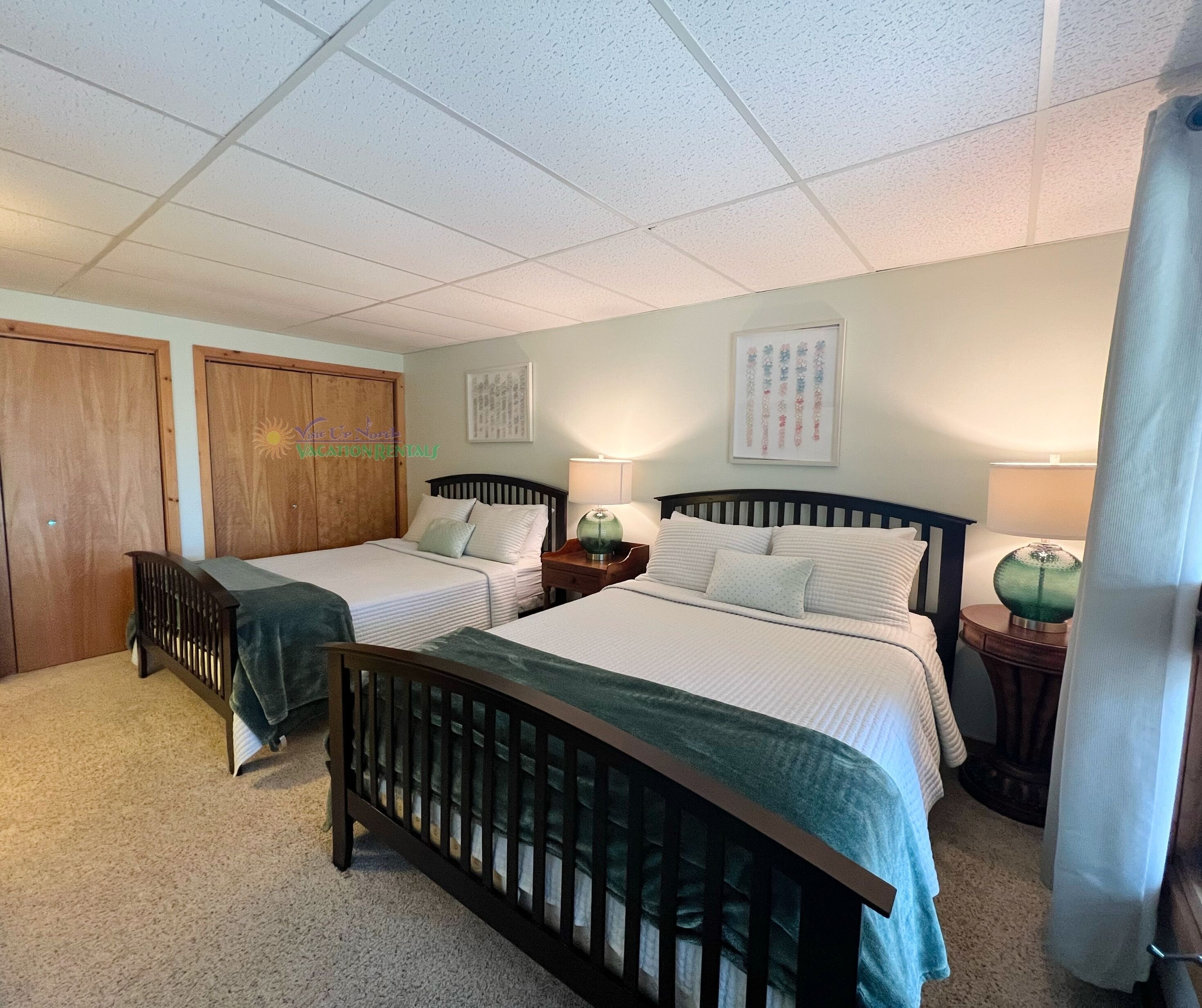 A bedroom with two beds, a wooden headboard, a nightstand with a lamp, and a wall-mounted artwork.