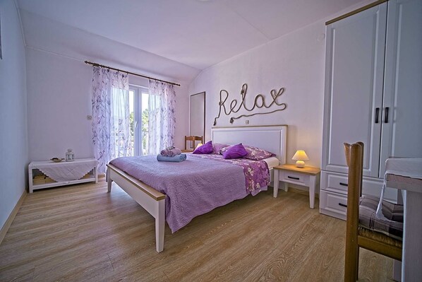 A bedroom with a bed, a nightstand, a bedside table, a chair, a wardrobe, and a window with curtains.