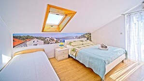 A bedroom with a skylight, a bed with a blue bedspread, a nightstand, and a view of a coastal town.