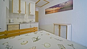 A compact bedroom with a bed, a small desk, a wardrobe, and a painting of a sunset on the wall.