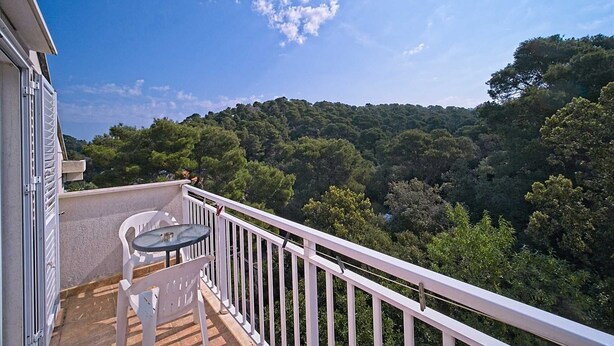 A balcony with a table and chairs, overlooking a forested hillside.