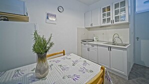 Cocina compacta con armarios blancos, un lavabo y una mesa de comedor con mantel floreado.