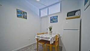 Una cocina pequeña con una mesa, sillas, un refrigerador y dos cuadros colgados en la pared.