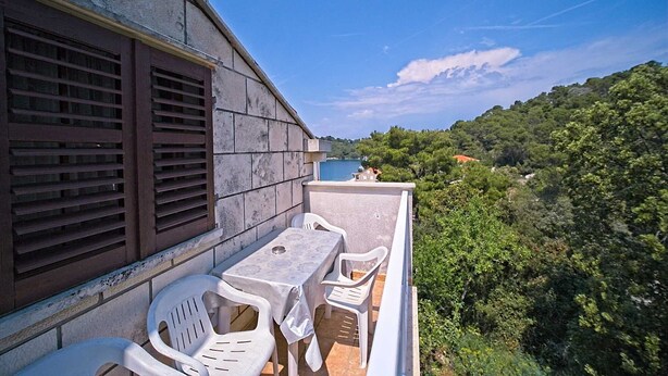 Ein Balkon mit Tisch und Stühlen mit Blick auf einen See und bewaldete Hügel.