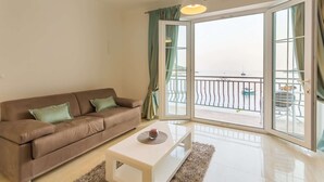 A modern living room with a brown sofa, a white coffee table, and a view of the sea through a glass door.