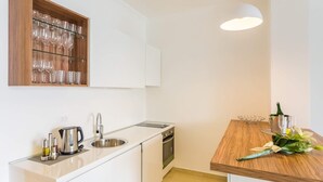 A modern kitchen with white cabinets, a wooden wine rack, a sink, a kettle, and a dining table with a bouquet of flowers.
