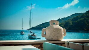A stone jug on a terrace overlooking a coastal scene with sailboats.